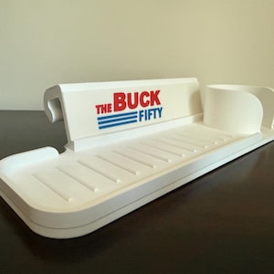 May include: A white plastic kitchen sink organizer with the text "THE BUCK FIFTY" in red and blue. The organizer has a slotted tray, a cup holder, and a raised back.