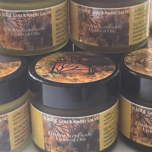 May include: Four small glass jars of goldenrod salve with black lids. Each jar has a label with a butterfly and the text "Seashore Goldenrod Salve" and "Herbal Scent with Essential Oils".