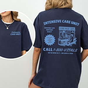 May include: Navy blue t-shirt with the text "Intensive Care Unit" on the front and back. The back of the shirt features a light blue graphic with the text "Code Blue Cafe" and "Call 1-800-VITALS".