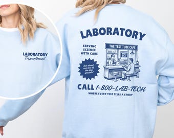 May include: Light blue sweatshirt with "LABORATORY" printed on the back, along with "THE TEST TUBE CAFE" graphic and "CALL 1-800-LAB-TECH". The front has "LABORATORY Department" in script. A casual, science-themed apparel item.