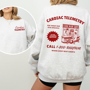 May include: A light gray sweatshirt with the words "Cardiac Telemetry" in red on the front and back. The back features a retro-style graphic with the text "Code Blue Cafe" and a phone number.
