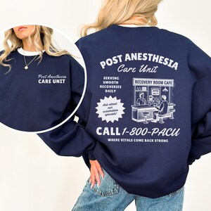 May include: Navy blue sweatshirt with white text. The front reads "Post Anesthesia Care Unit." The back features a graphic of a cafe and text that says "Post Anesthesia Care Unit" and "Call 1-800-PACU."