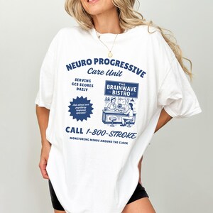 May include: White t-shirt with a blue graphic that reads "NEURO PROGRESSIVE Care Unit" and "The Brainwave Bistro." The shirt also has the phone number "1-800-STROKE" and the phrase "MONITORING MINDS AROUND THE CLOCK."