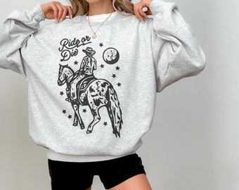 Puede incluir: Sudadera gris con un gráfico en blanco y negro de una vaquera montando un caballo. El gráfico incluye el texto "Ride or Die" y estrellas.
