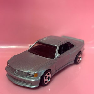 May include: A silver toy car model of a Mercedes-Benz 500E.