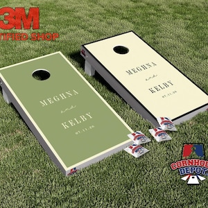 Può includere: Due tavole da cornhole personalizzate con i nomi "Meghna e Kelby" e la data 07.11.20. Una tavola è verde oliva, l'altra color crema. Quattro sacchi di fagioli sono davanti alle tavole. Le tavole sono su una superficie erbosa verde.