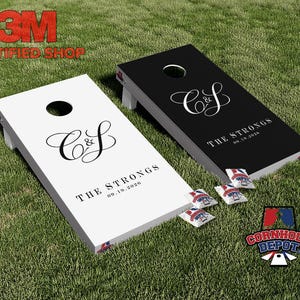 Può includere: Due tavole da cornhole personalizzate, una bianca e una nera, con le iniziali "C&S", il nome "The Strongs" e la data "09.19.2026". Include sacchi di fagioli con un design patriottico. Le tavole sono su un prato verde.