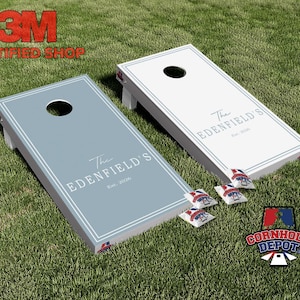 May include: Two cornhole boards, one light blue and one white, with the text "The Edenfield's Est. 2026". Each board has a centered hole and is surrounded by a white border. Four bean bags and a logo are also visible.
