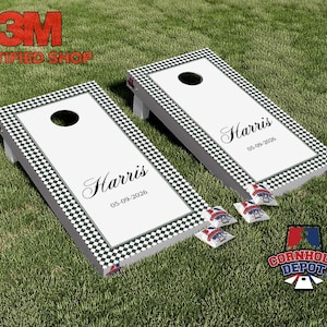 May include: Two cornhole boards with a white surface and a black and white checkered border. Each board has a centered hole and the name "Harris" with the date "05-09-2026". Several bean bags are visible.