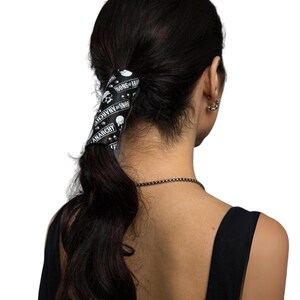May include: Black leather ponytail holder with silver studs and a skull design. The holder has the text "Sons of Anarchy" and "Anarchy" printed on it.