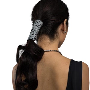 Peut inclure: Un élastique à cheveux noir et blanc avec un motif géométrique. L'élastique est porté en queue de cheval.