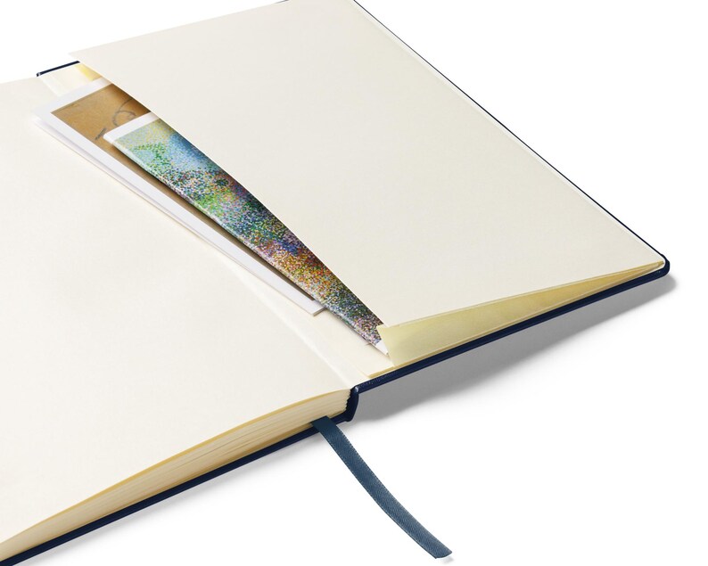 May include: A navy blue hardcover journal with a cream-colored interior and a ribbon bookmark. The journal has a pocket on the inside cover.