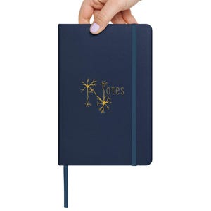 May include: A dark blue notebook with a gold neuron illustration and the word "Notes" printed on the cover. The notebook has a blue ribbon bookmark.