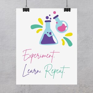 May include: A white poster with a colorful illustration of two beakers and the text "Experiment. Learn. Repeat."