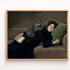 May include: A framed vintage painting depicts a woman reclining on a sofa with a gray cat. She wears a black dress and holds a book. Green pillows provide support. The artwork has a classic, timeless aesthetic.