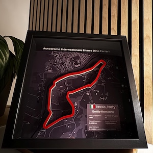 Könnte beinhalten: Eine gerahmte Schwarzweißkarte der Rennstrecke Autodromo Internazionale Enzo e Dino Ferrari in Imola, Italien. Die Strecke ist rot hervorgehoben. Der Text "Imola, Italien" und "'Emilia-Romagna'" ist auf der Karte abgebildet. Der Text "Erster Grand Prix 1980", "Streckenlänge 4,909 km", "Anzahl der Runden GT", "Rennstrecke 301,049 km", "Rundenrekord 1.15.484 Lewis Hamilton (2020)" ist ebenfalls abgebildet.