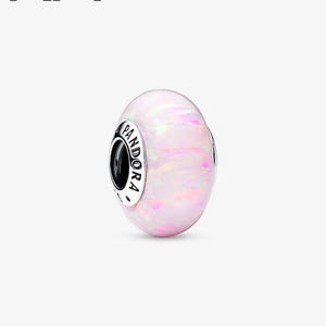 May include: A pale pink bead with shimmering highlights. The bead is spherical and features a silver band with the word "PANDORA" in black text. This is a jewellery item.