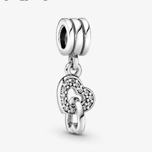 May include: A silver charm featuring two interlocking hearts. One heart is embellished with small, clear gemstones. The charm has a three-ringed top for attachment. The letters "KA" are in the upper left corner.