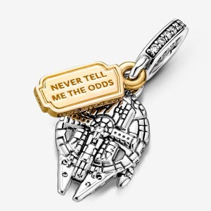 May include: A silver and gold charm with a Millennium Falcon design. The charm has a gold tag with the text "NEVER TELL ME THE ODDS" and a silver band with clear stones.