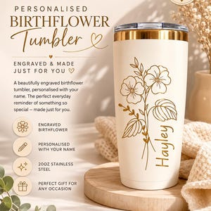 May include: A cream-colored 20oz stainless steel tumbler with a gold-toned rim and a clear lid. The tumbler features a gold-colored engraved floral design and the name Hayley. Text on the image includes The Honey Pot Shop, Personalised Birthflower Tumbler, and Made with love. Made for you.
