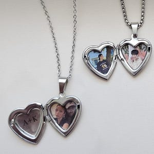 May include: Several silver heart-shaped locket necklaces with photos inside. The lockets are open, revealing the pictures. The necklaces have silver chains. One locket has the initials "A+K" engraved on it.