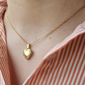 May include: A gold chain necklace with a heart-shaped locket pendant.