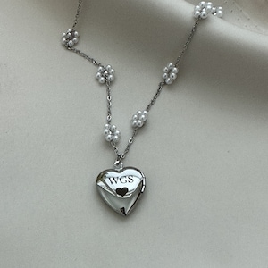 May include: A silver heart-shaped locket necklace with a pearl chain and the inscription "WGS" on the front.