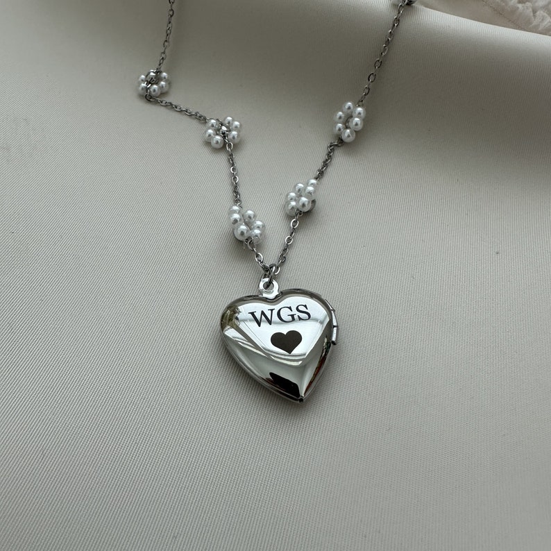 May include: A silver heart-shaped locket necklace with a pearl chain. The locket has the initials "WGS" engraved on it and a small heart inside.