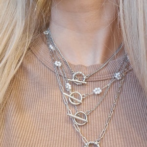May include: A layered silver necklace with multiple toggle clasps and small pearl accents.