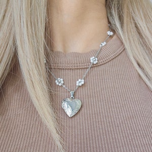 May include: A silver necklace with a heart-shaped locket and small pearl flower accents.