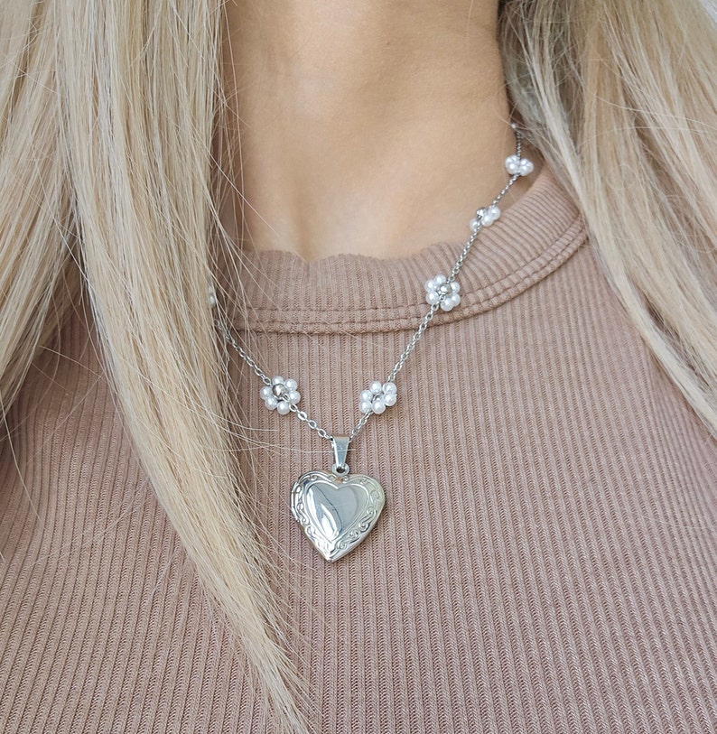 May include: A silver necklace with a heart-shaped locket and small pearl flower accents.