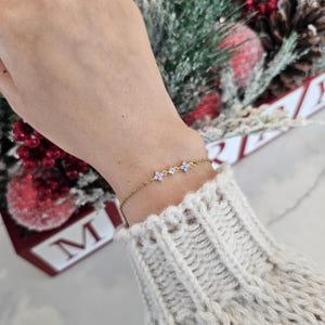 May include: A delicate gold chain bracelet with three small flower charms, each adorned with tiny white stones.