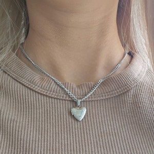 May include: A silver chain necklace with a heart-shaped locket pendant.
