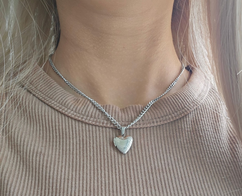 May include: A silver chain necklace with a heart-shaped locket pendant.