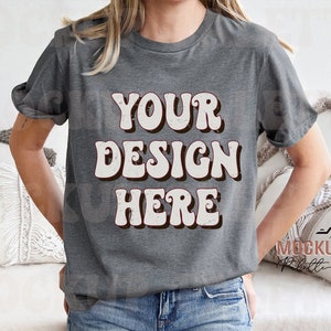 May include: A gray t-shirt with the text "YOUR DESIGN HERE" in a retro font. The text is white with a distressed look.