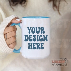May include: White ceramic mug with a blue rim and handle. The mug has the text "YOUR DESIGN HERE" printed in blue on the front.
