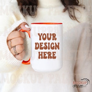 May include: White ceramic mug with an orange rim and handle. The mug has the text "YOUR DESIGN HERE" in brown letters with a distressed look.