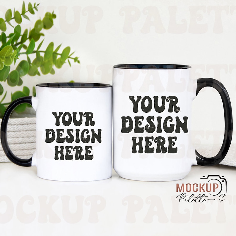 May include: Two white ceramic mugs with black rims and handles. Both mugs have the text "YOUR DESIGN HERE" in black, stylized lettering. The mugs are on a white surface.