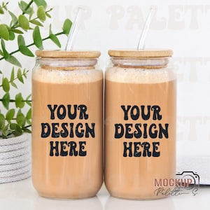 May include: Two clear glass mugs with bamboo lids and straws. The mugs are filled with a brown liquid and have the text "Your Design Here" printed on them.