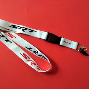 May include: White lanyard with a black plastic clip and a silver key chain. The lanyard has the word "SRT" printed in red and black letters.