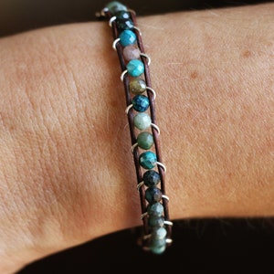 May include: A brown leather bracelet with silver accents and a row of turquoise, green, and brown gemstone beads.