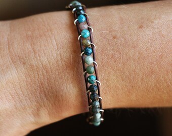 May include: A brown leather bracelet with silver accents and a row of turquoise, green, and brown gemstone beads.