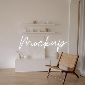 May include: A white cabinet with three drawers and a white canvas painting on top. A wicker chair with a wooden frame sits in front of the cabinet. The wall behind the cabinet is white and has two shelves with decorative items on them. The text "Mockup" is written in white on the wall.
