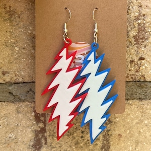 May include: A pair of earrings featuring a lightning bolt design. The earrings are made of white acrylic and are painted in red and blue.