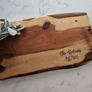May include: A large wooden serving tray with natural wood grain and two brass handles. The tray is engraved with the text "The Garcins Est 1990".