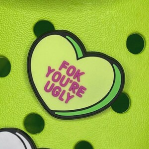 Może przedstawiać: Zielony charm w kształcie serca z różowym napisem "FOK YOU'RE UGLY".