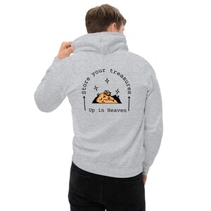Könnte beinhalten: Ein grauer Hoodie mit einem Aufdruck auf der Rückseite, der "Store your treasures up in Heaven" lautet. Der Aufdruck zeigt einen Haufen Goldmünzen mit einer Krone darauf.