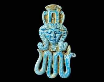 May include: A blue glazed ceramic amulet depicting the Egyptian goddess Wadjet, with a cobra head and a human face. The amulet is in the form of a pendant.