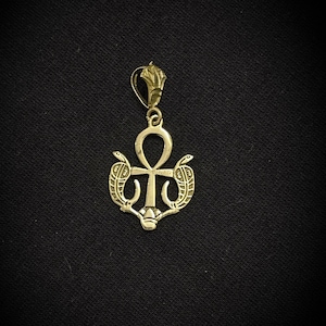 以下が含まれることがあります： 2匹のヘビが巻き付いたアンクのシンボルが描かれたゴールドのペンダント。ペンダントは細部までこだわったデザインで、どんな服装にも古代エジプトのスタイルを加えるのに最適です。
