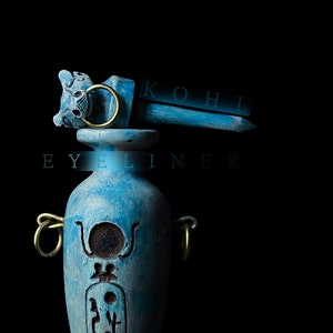 Puede incluir: Un tarro de cerámica azul con tapa dorada y un diseño decorativo. El tarro está etiquetado como "KOHL EYELINER".